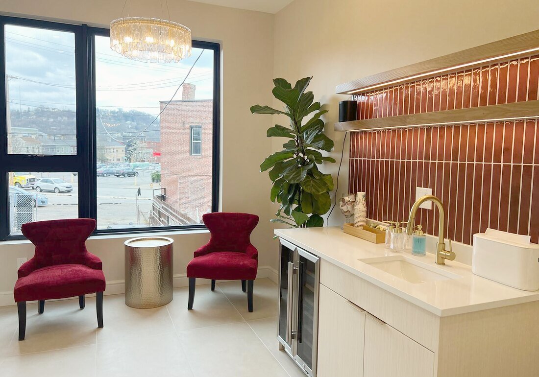 The Lawrenceville waiting lounge — burgundy velvet chairs under a brass chandelier, beside the fluted oxblood wall