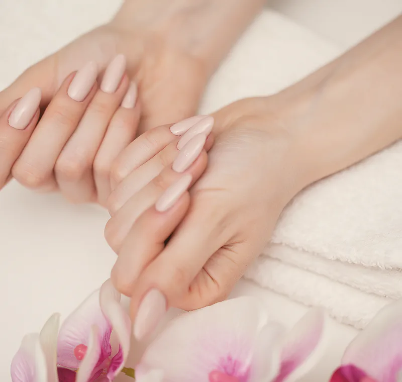 A strengthened natural nail in a long almond shape, finished in a nude shade