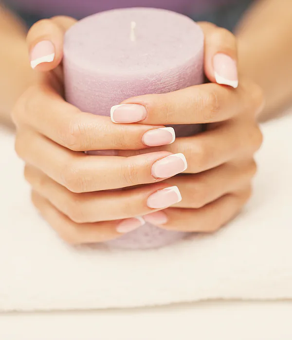 Hands with a pale manicure cupped around a lit candle